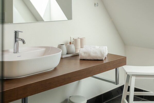 A modern bathroom with a large white sink, a mirror, and a wooden vanity.