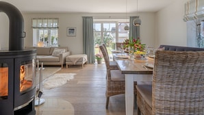 A cozy living room with a fireplace, a dining area with wicker furniture, and a view of the outdoors.