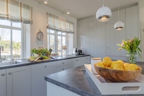 Une cuisine moderne dotée d’un grand îlot central, de meubles blancs et offrant une vue sur l’extérieur.