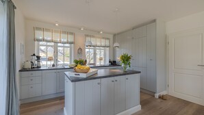 A modern kitchen with grey cabinetry, a central island, and a window with striped curtains.