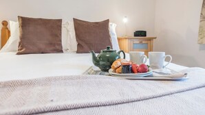 En pænt redt seng med brune puder, en grøn tepotte, croissanter, jordbær og hvide kopper på et fad.