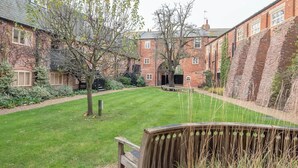 A courtyard with a grassy lawn, a wooden bench, and a tree with green leaves. - Kiln House, Snape Maltings (Snape)