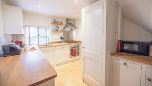 A modern kitchen with white cabinets, a wooden countertop, a stainless steel range hood, a microwave, and a toaster. - Kiln House, Snape Maltings (Snape)