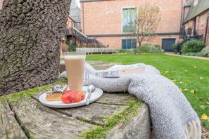 A wooden table with a glass of a beverage, a plate with a dessert and strawberries, and a book titled "How to be Happy" by Eva Woods. - Kiln House, Snape Maltings (Snape)