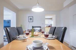 A dining area with a wooden table set for four, surrounded by black chairs, a white pendant light, and a framed picture on the wall. - Kiln House, Snape Maltings (Snape)