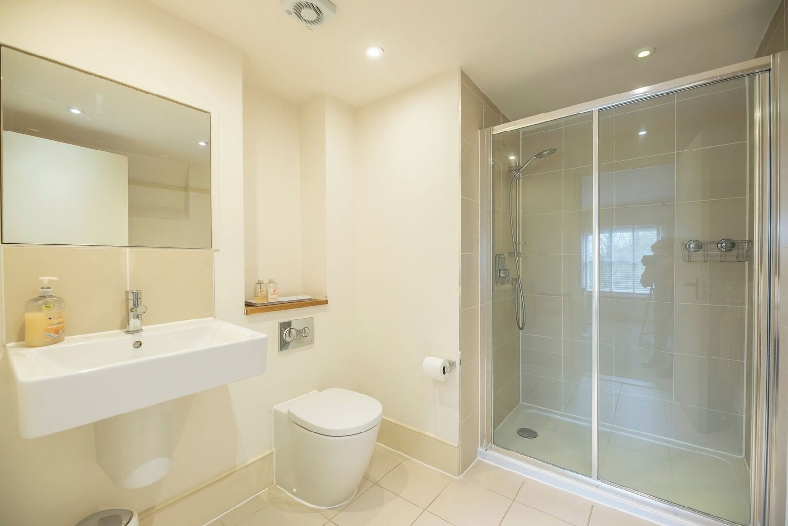 A modern bathroom with a glass-enclosed shower, a white sink with a mirror above it, and a toilet.