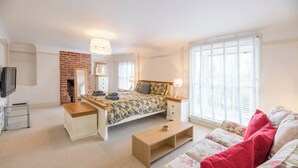 A bedroom with a bed, bedside table, lamp, and a TV. - Kiln House, Snape Maltings (Snape)