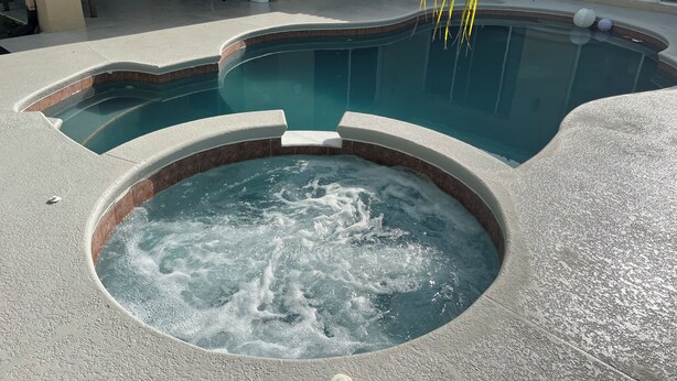A swimming pool with a hot tub in the center, surrounded by a patio area with chairs and a door.