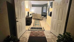 A hallway leading to a living room with a sofa, a coffee table, and a lamp. There are two potted plants on either side of the hallway.