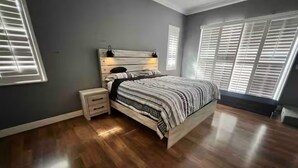 A bedroom with a wooden bed, bedside tables, and a window with blinds.