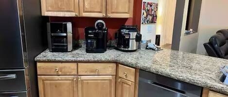 A kitchen with wooden cabinets, a granite countertop, a refrigerator, a dishwasher, and a coffee maker.