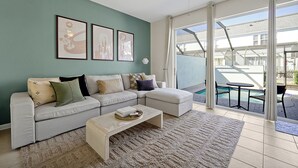 Ein Wohnzimmer mit einer Couch, einem Couchtisch und Blick auf einen Swimmingpool durch große Glasschiebetüren.