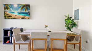 Ein Essbereich mit einem Tisch für zwei Personen, umgeben von Stühlen, einem Bücherregal und einem großen Gemälde mit Strandmotiv.