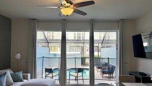 Ein Hotelzimmer mit Deckenventilator, einer Sitzecke, einem Esstisch und Blick auf einen Außenpoolbereich.