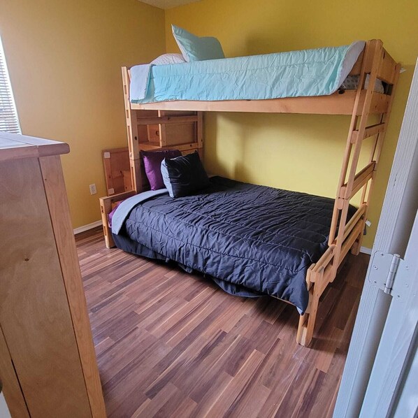 Un lit superposé avec un matelas et des oreillers bleus, une commode en bois et un plancher en bois.