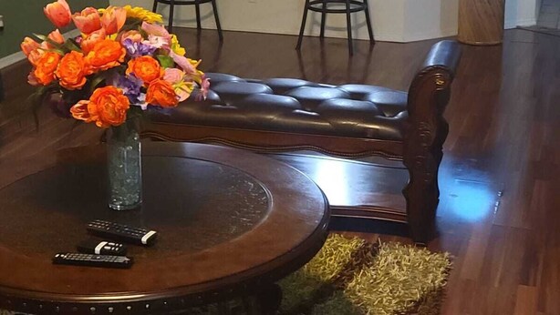 Un área de comedor con una mesa redonda, dos taburetes de bar, un florero y una barra con dos sillas.