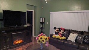 Una sala de estar con chimenea, televisor, un sofá con peluches y un jarrón de flores.