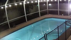 Una piscina con cerramiento de vidrio, rodeada por una barandilla metálica.