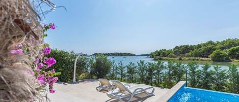 A pool area with two lounge chairs and a view of a lake and forest.