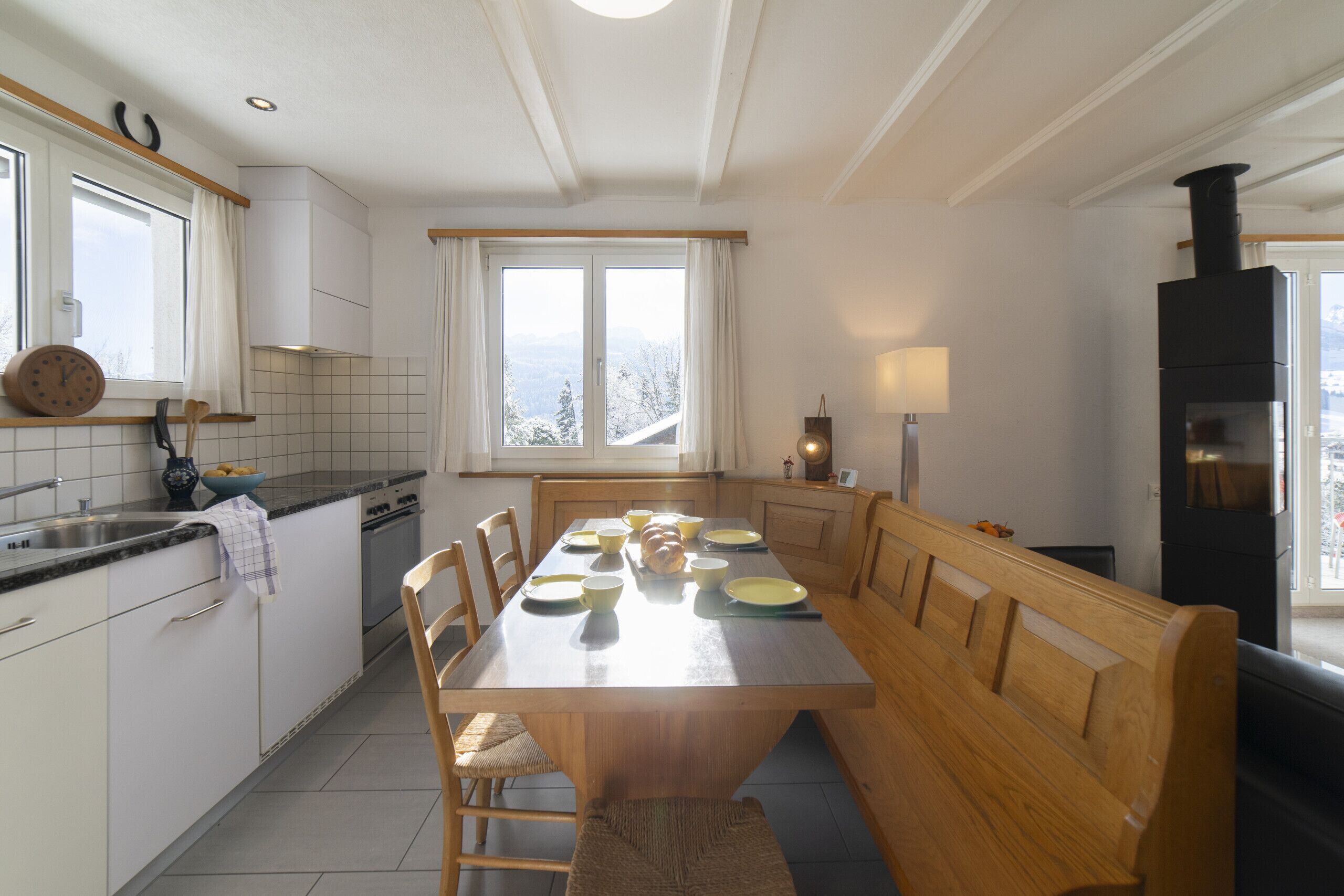 A modern kitchen with a central island, wooden benches, and a view of the outdoors.