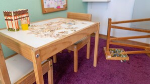 Una mesa de madera con piezas de un rompecabezas, una casa de juguete y un cerdito de juguete a la izquierda.