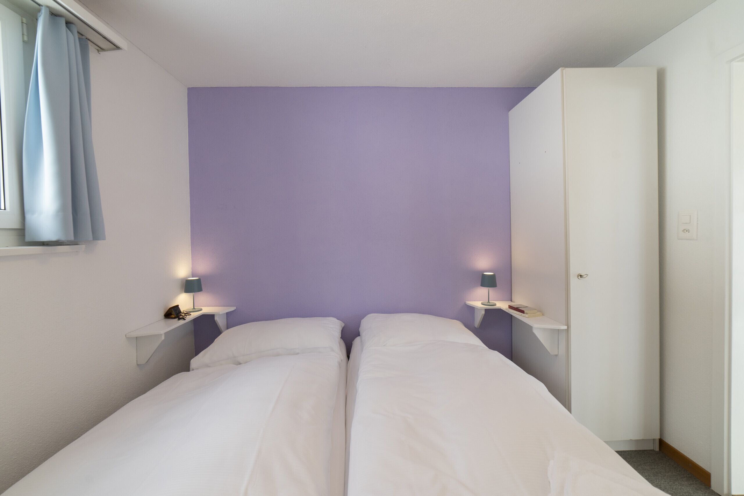 A bedroom with two beds, a wardrobe, and bedside lamps.