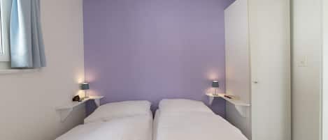 A bedroom with two beds, a wardrobe, and bedside lamps.