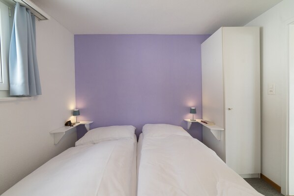 A bedroom with two beds, a wardrobe, and bedside lamps.