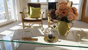 Una mesa con cubierta de vidrio, un tablero de Scrabble, una taza de café y un jarrón con flores.