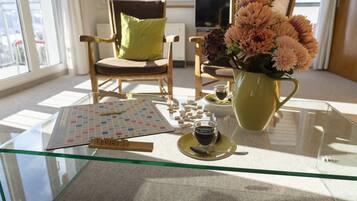 Ein Tisch mit Glasplatte, ein Scrabble-Spiel, eine Kaffeetasse und eine Blumenvase.