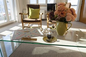 Una mesa con cubierta de vidrio, un tablero de Scrabble, una taza de café y un jarrón con flores.