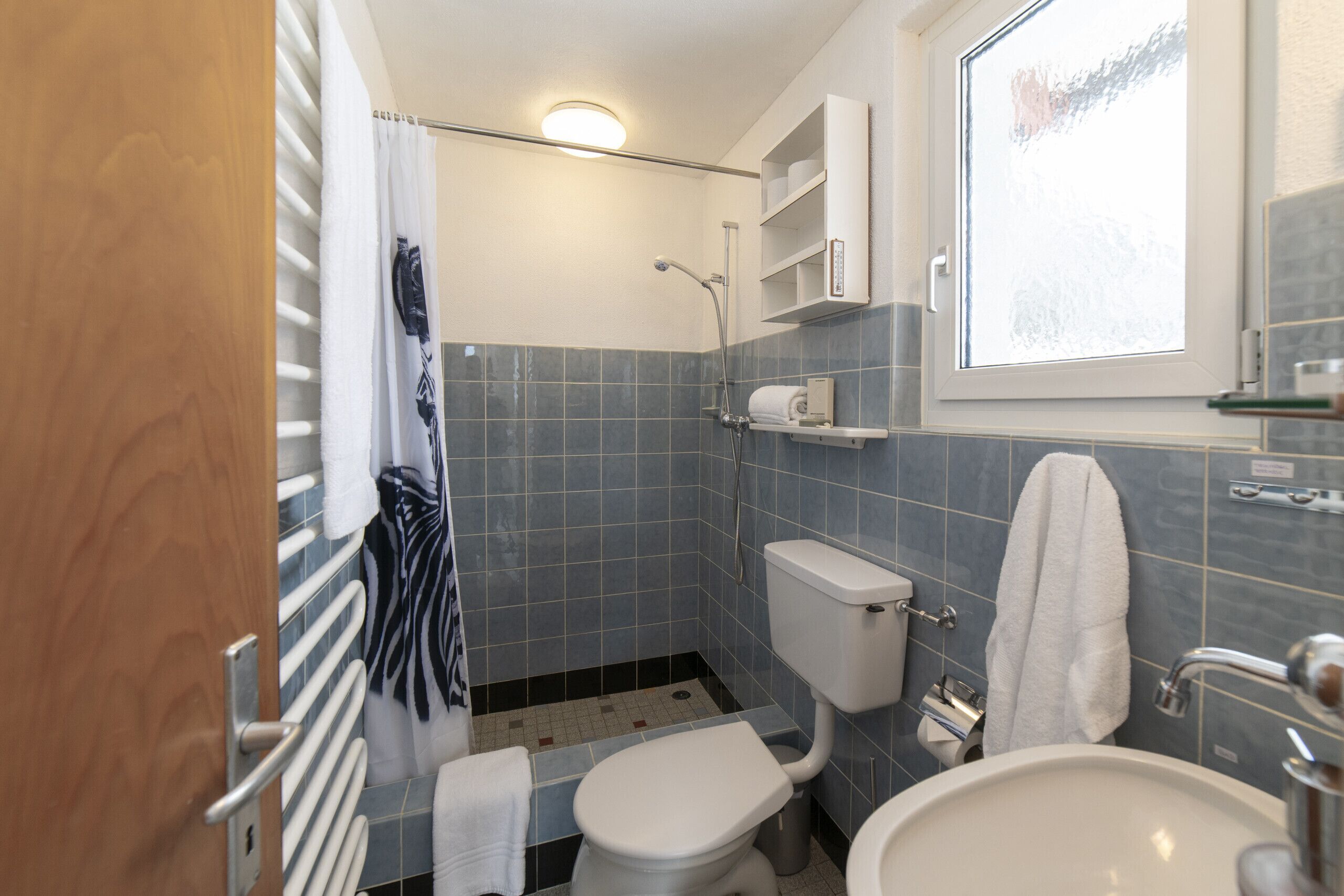 Ein kleines Badezimmer mit Toilette, Bidet und Waschbecken, ausgestattet mit blauen Fliesen und einem Fenster.