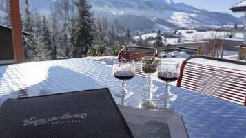 A table with two wine glasses and a menu on a glass table with a mountain view in the background.