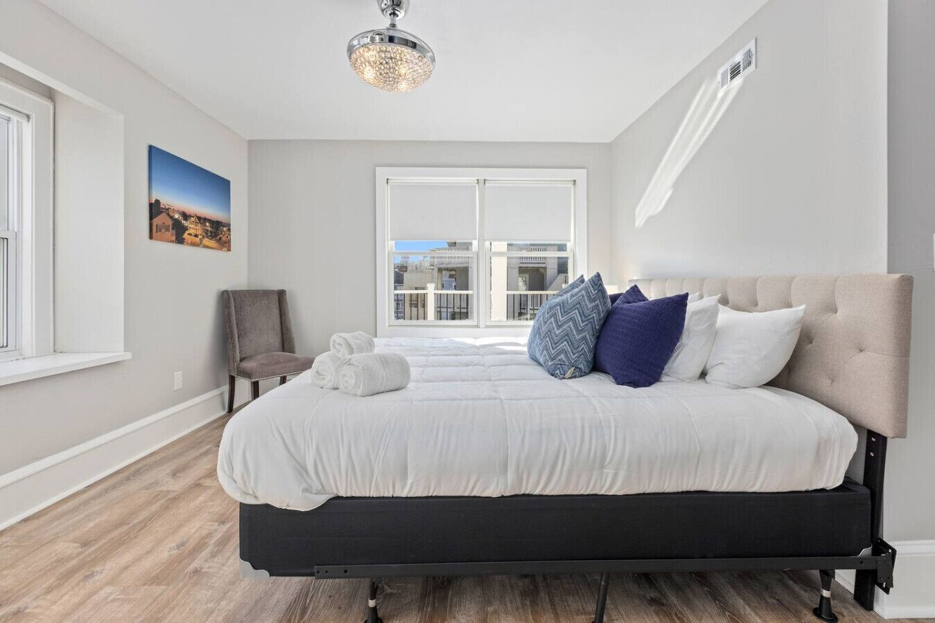 Un dormitorio moderno con una cama grande, una silla gris, una ventana con vista a la ciudad y una lámpara en el techo.