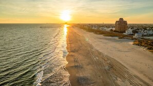 A beach with a sunset, a pier, and buildings along the shore.