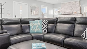 A modern living room with a black leather sectional sofa, a grey ottoman, and decorative pillows.