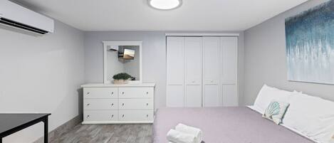A modern bedroom with a bed, dresser, and a large window.