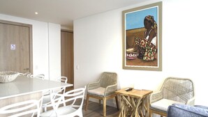 A modern room with a dining table, white chairs, a wicker sofa, and a framed painting on the wall. - Modern new 3 bedroom apartment 5min walk to beachl/shops/restaurants (San Andrés)