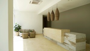 A modern reception area with a light-colored reception desk, a potted plant, and a seating area with two stools. - Modern new 3 bedroom apartment 5min walk to beachl/shops/restaurants (San Andr és)