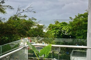 Une vue depuis un balcon doté d’une balustrade, donnant sur une étendue d’eau et une végétation luxuriante.