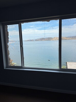 A window with a view of a calm body of water, a distant shoreline, and a clear sky.