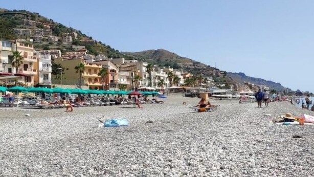 A pebble beach with buildings in the background and people sunbathing. - Casa del Mare Sicily Letojanni  (Letojanni)