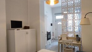 A bedroom with a bed, a TV on a cabinet, a dining area with a table and chairs, and a decorative screen. - Casa del Mare Sicily Letojanni  (Letojanni)