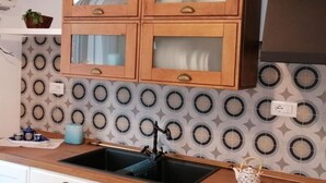 A kitchen with wooden cabinets, a black sink, and a patterned backsplash. - Casa del Mare Sicily Letojanni  (Letojanni)