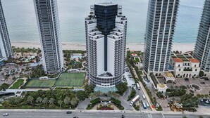 A high-rise hotel with a central courtyard, a beach view, and a tennis court. - LUXURIOUS APARTMENT FRONT OF THE BEACH IN SUNNY ISLE (Sunny Isles Beach)