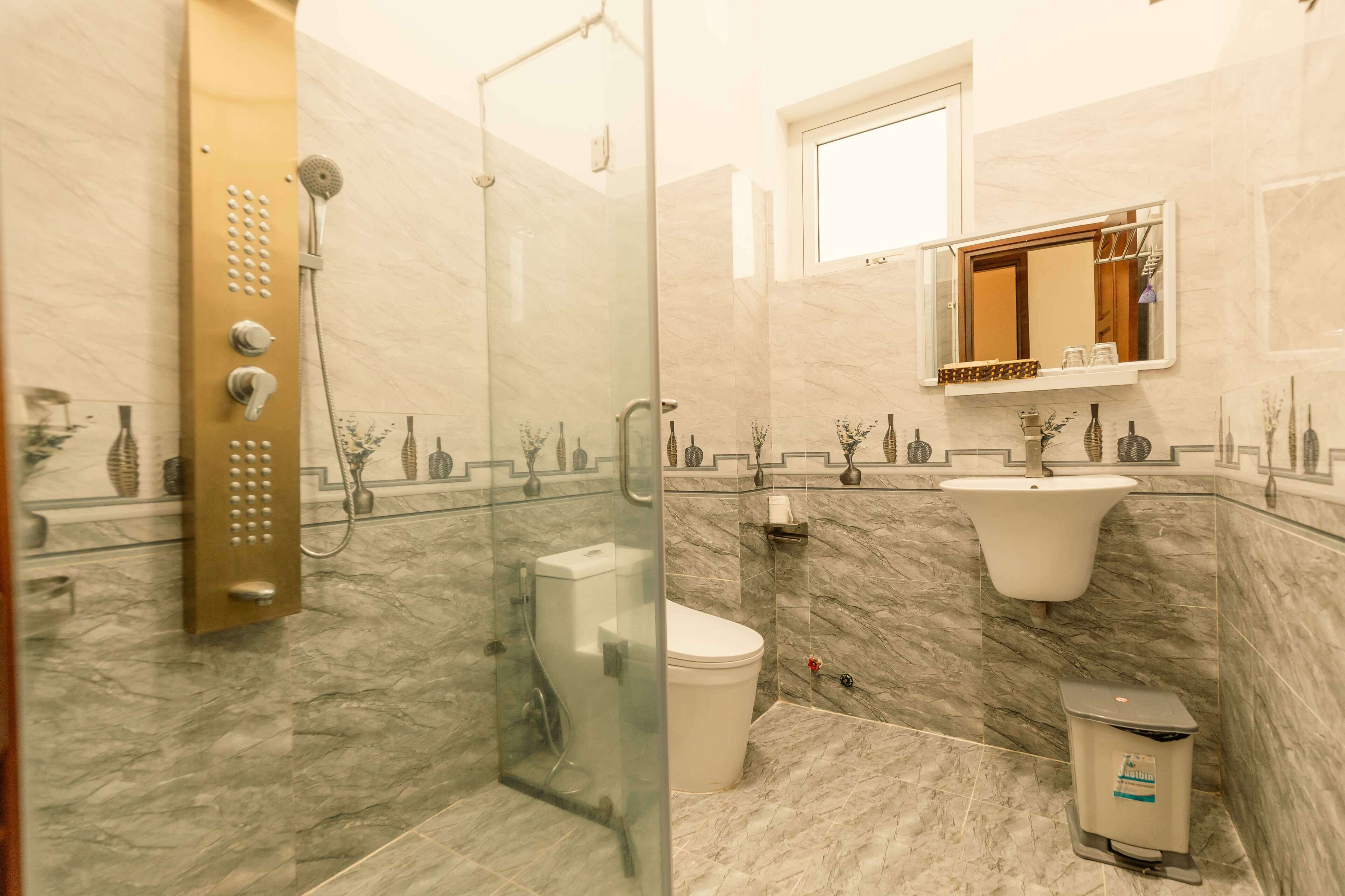 A modern bathroom with a glass-enclosed shower, a marble-tiled floor, a white toilet, and a sink with a mirror above it.