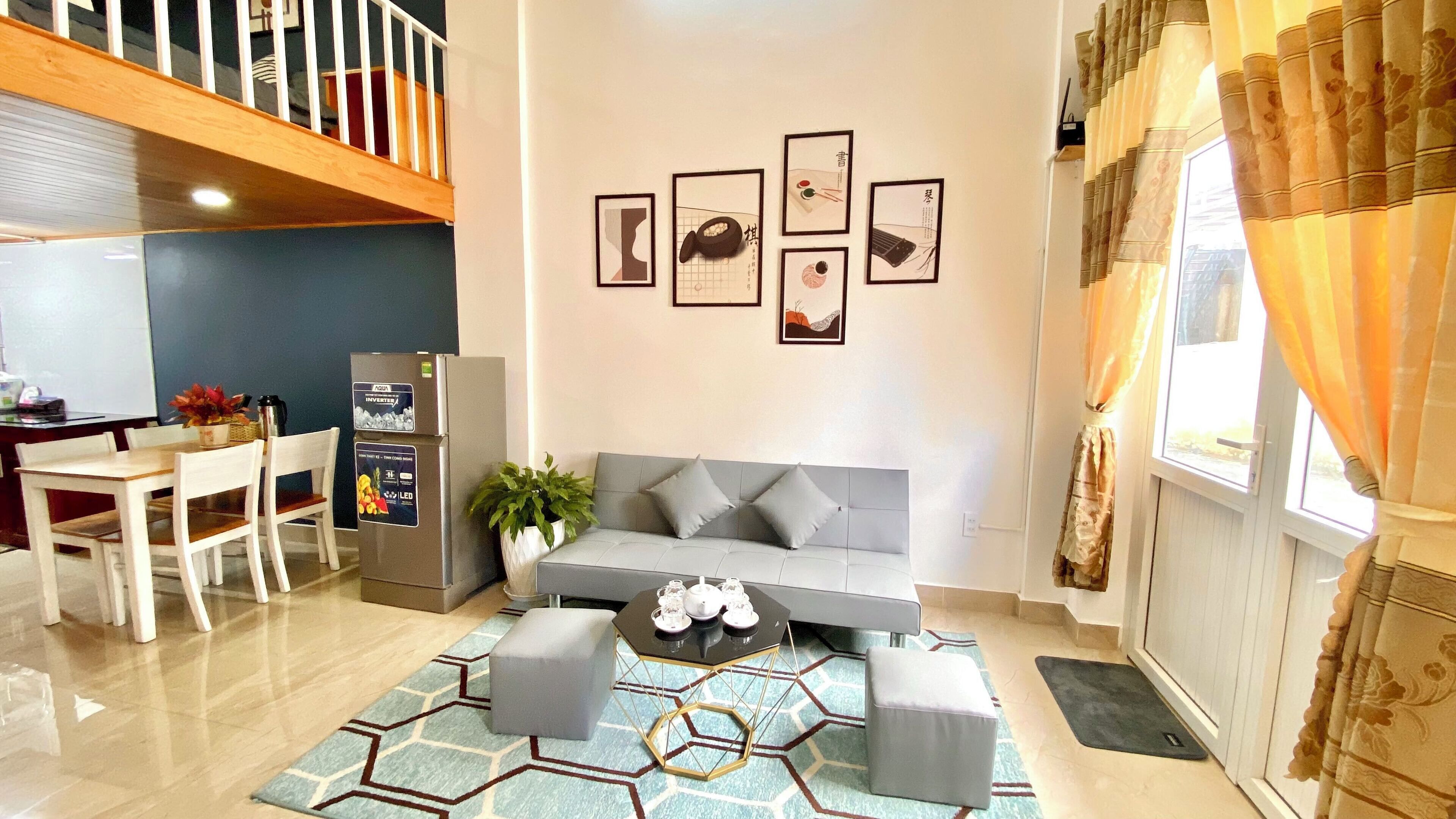 A modern living room with a grey sofa, a dining table with chairs, a coffee table, and a wall with framed pictures.