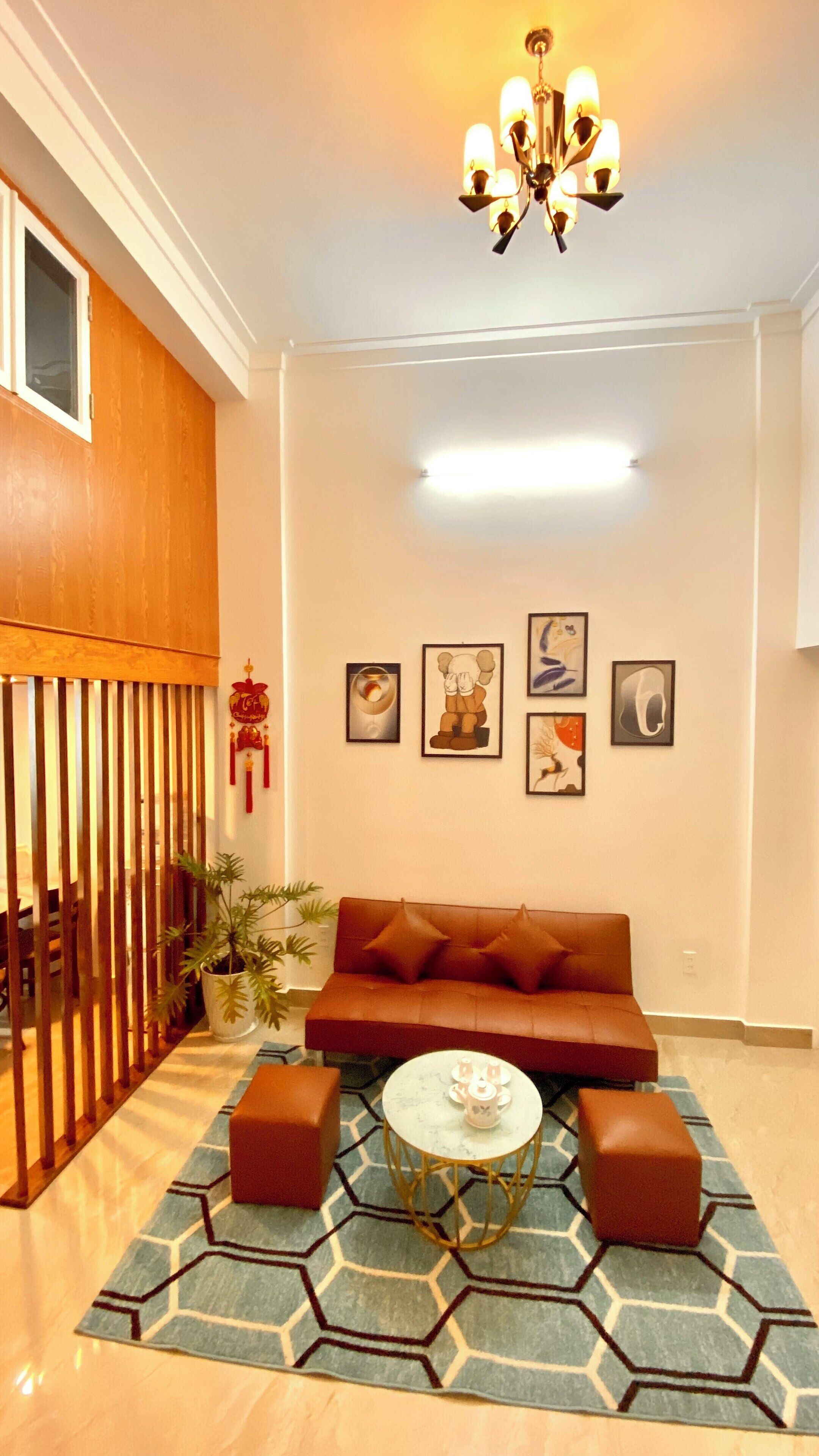 A living room with a sofa, two ottomans, a coffee table, and a chandelier. There are four framed pictures on the wall.