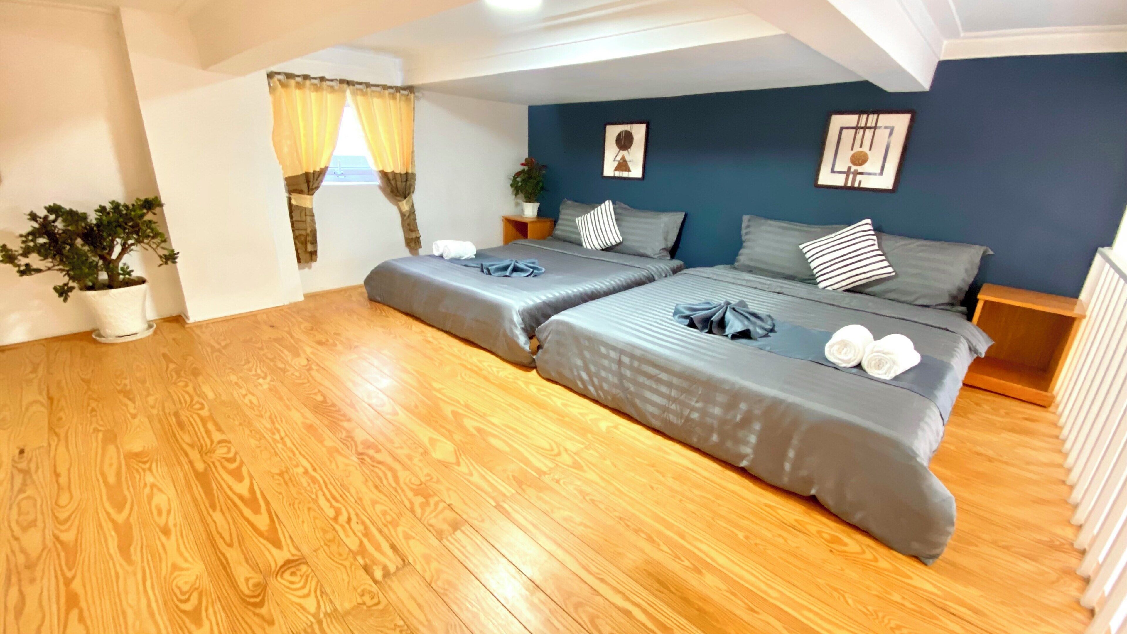 Une chambre avec deux lits, un plancher en bois, une fenêtre avec des rideaux et une plante en pot.