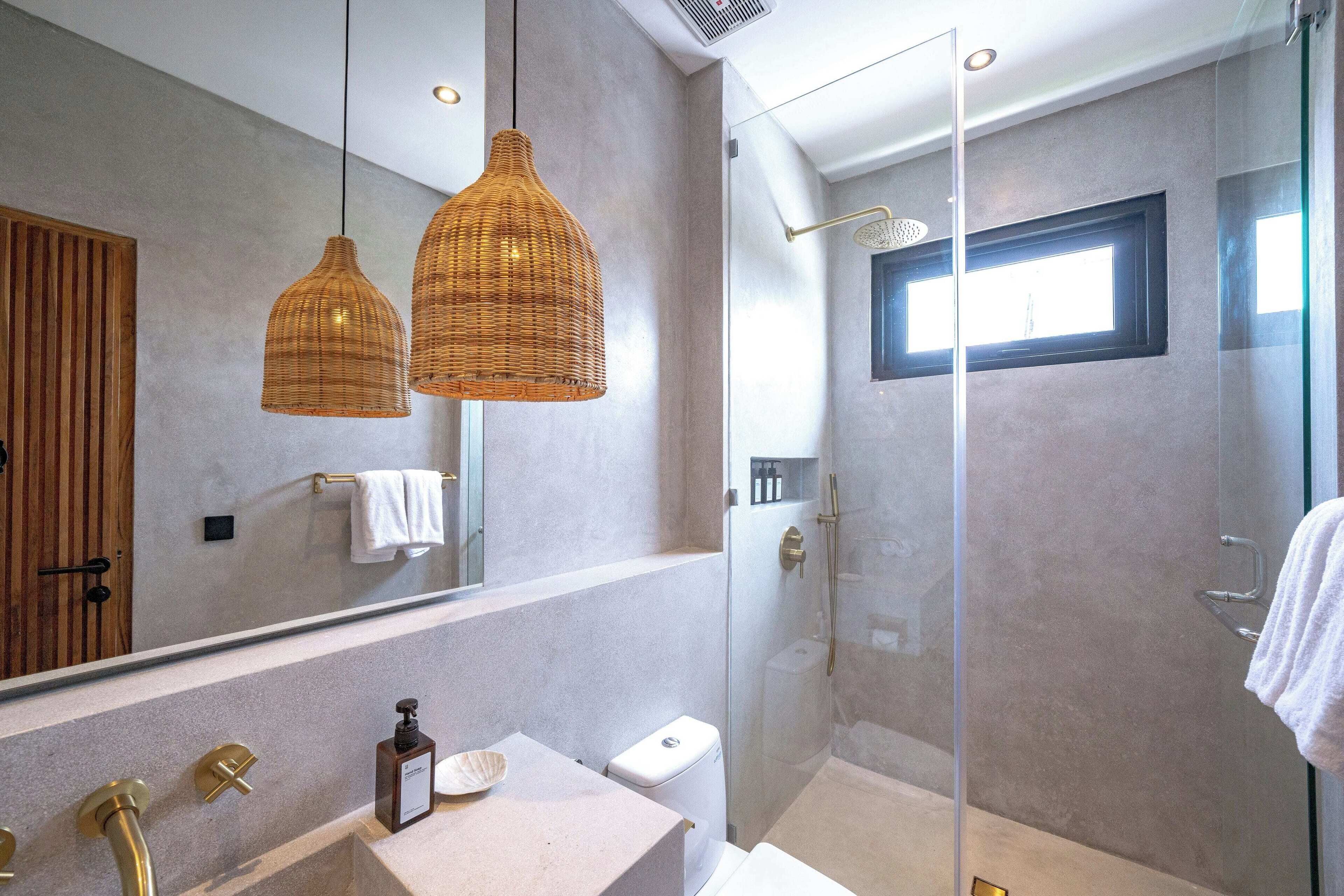 A modern bathroom with a glass shower enclosure, a large mirror, and two wicker pendant lights.